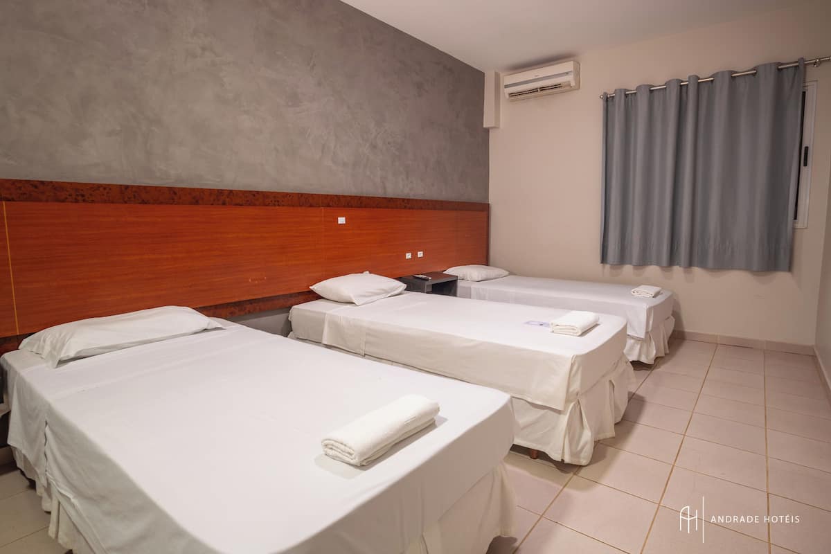 A hotel room with three beds, a wooden headboard, a grey curtain, and a tiled floor.