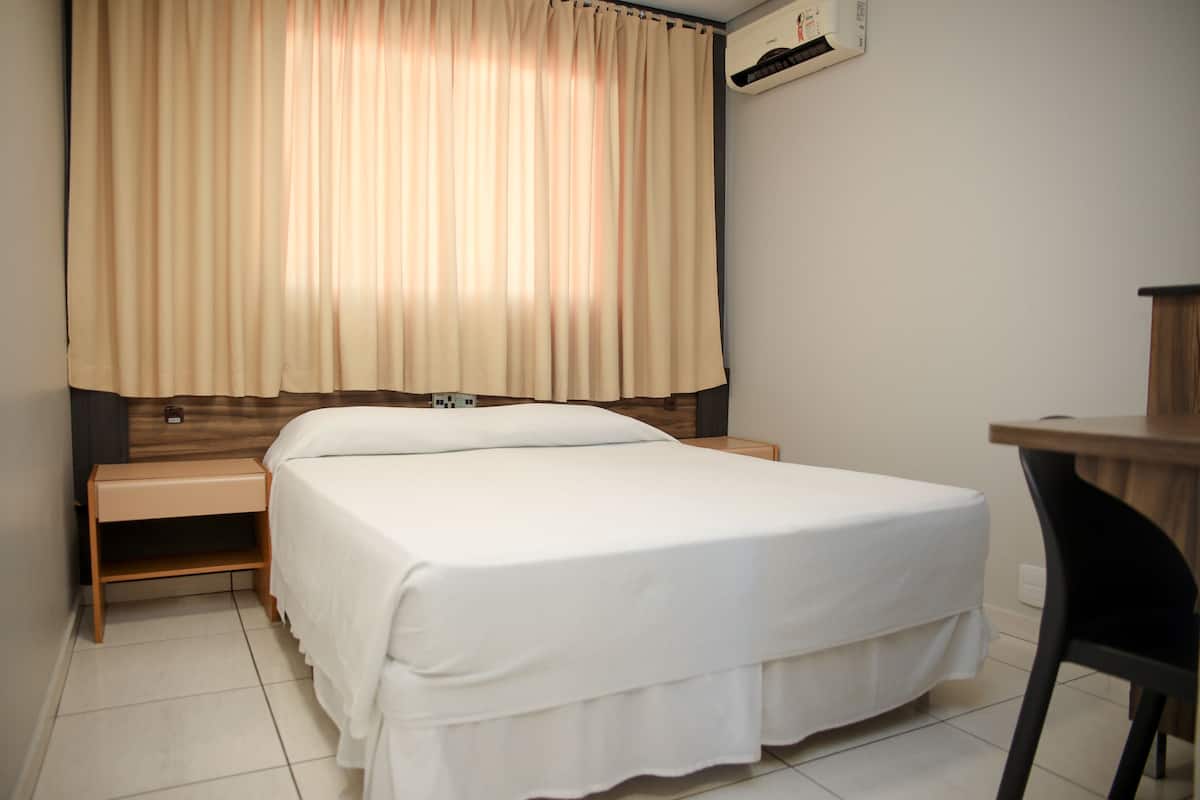 A hotel room with a bed, a nightstand, a desk, and a window with curtains.