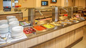 Buffet com diversas opções de comida, incluindo saladas e uma seleção de carnes, com pratos e talheres organizados no balcão.