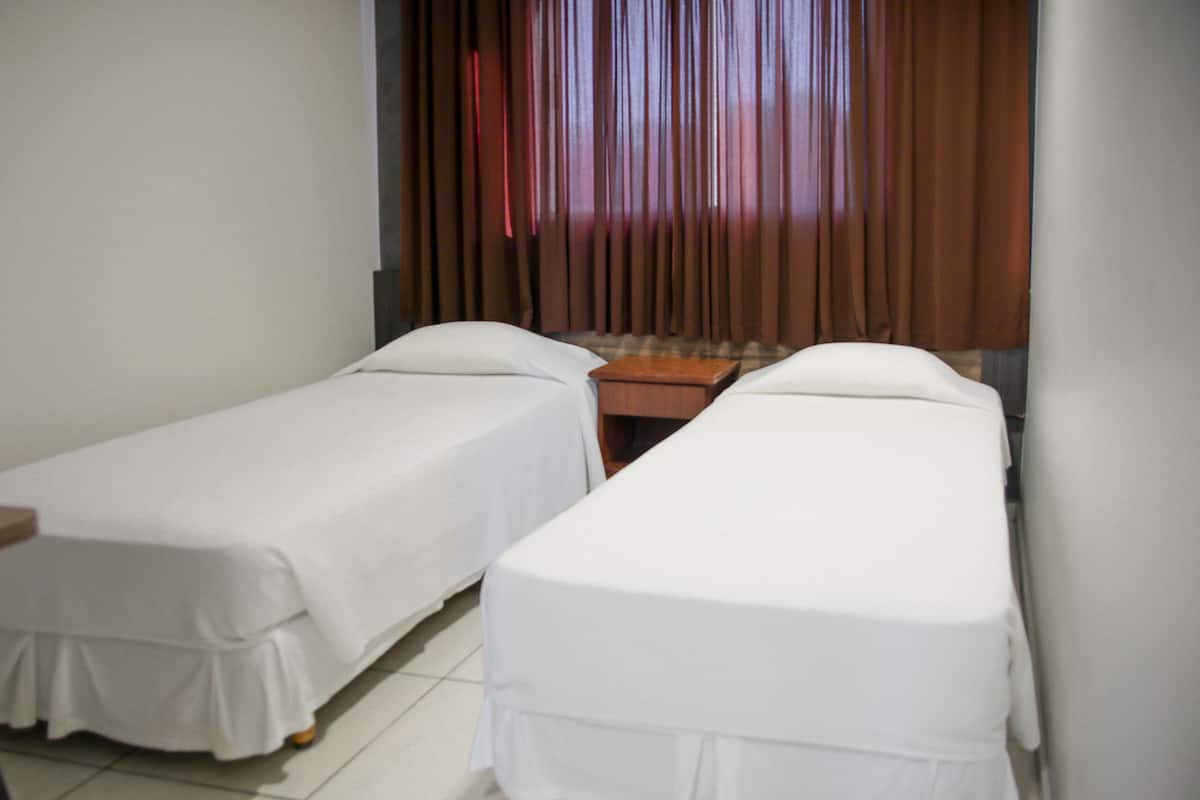 A room with two single beds, a small wooden table, and a window with curtains.