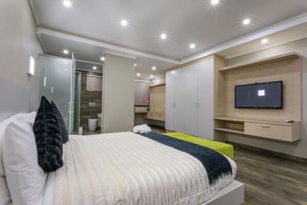 Une chambre à coucher moderne avec un lit, un téléviseur fixé au mur et un dressing.