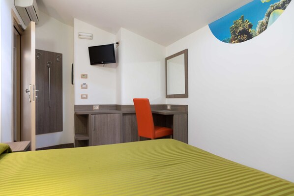 A hotel room with a bed, a desk, a chair, a TV, and a mirror.