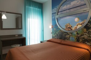 Habitación de hotel con cama, ventana redonda con vista al mar, espejo y cortina azul.