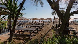 Ein Restaurant am Strand mit Terrassensitzgelegenheiten, Sonnenschirmen und Meerblick.