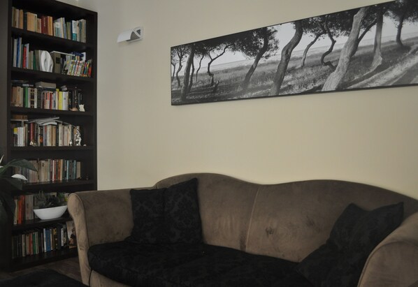 Una sala de estar con un sofá, una estantería y un cuadro de paisaje en la pared.