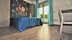 Ein Schlafzimmer mit einem Bett, das mit einer blauen Decke bezogen ist, einer Wandmalerei, einer Glastür zum Außenbereich und einem Sessel.
