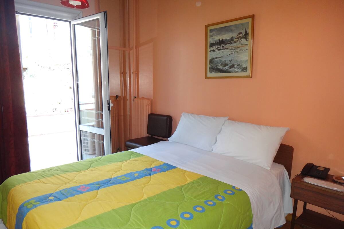A hotel room with a bed, a nightstand, a painting on the wall, and a view through the window.