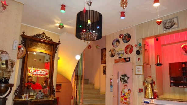 Un pasillo con una escalera, un candelabro y varias decoraciones, incluyendo un cartel de Harley-Davidson y una figura de Papá Noel.