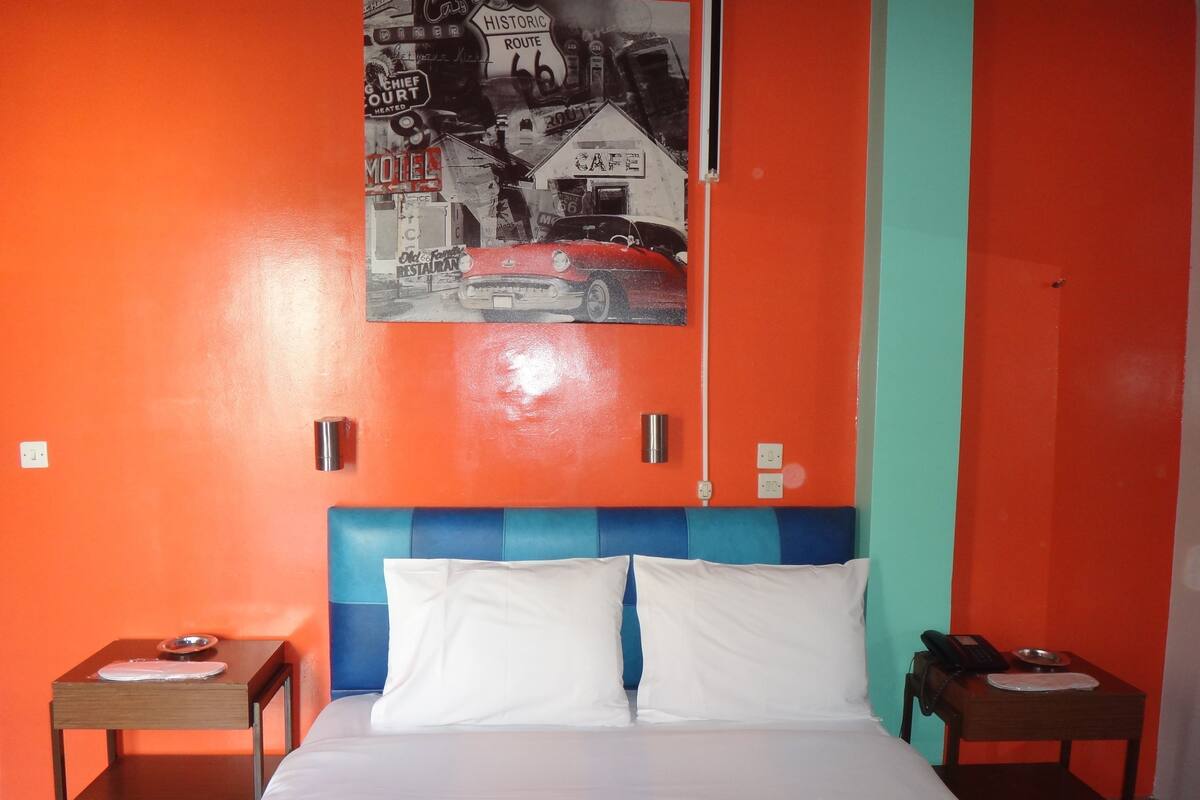A hotel room with a bed, two bedside tables, a wall-mounted telephone, and a poster on the wall.