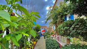 A narrow cobblestone pathway flanked by lush greenery and a building with blue accents. - Kayezta Hotel Alacati (Cesme)