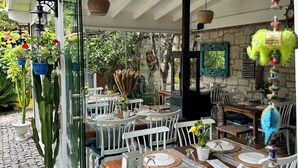 An outdoor dining area with white chairs and tables, a cactus plant, and hanging baskets. - Kayezta Hotel Alacati (Cesme)