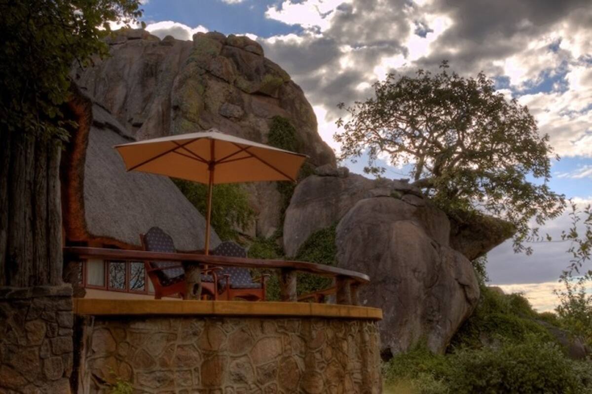 Un balcon en pierre, agrémenté d’une table et de chaises, qui offre une vue sur un paysage rocheux et un arbre.