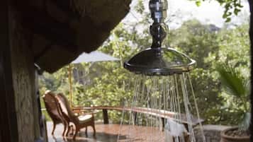 Un cabezal de ducha con agua corriendo, una silla de madera y una pared de piedra en un jardín.