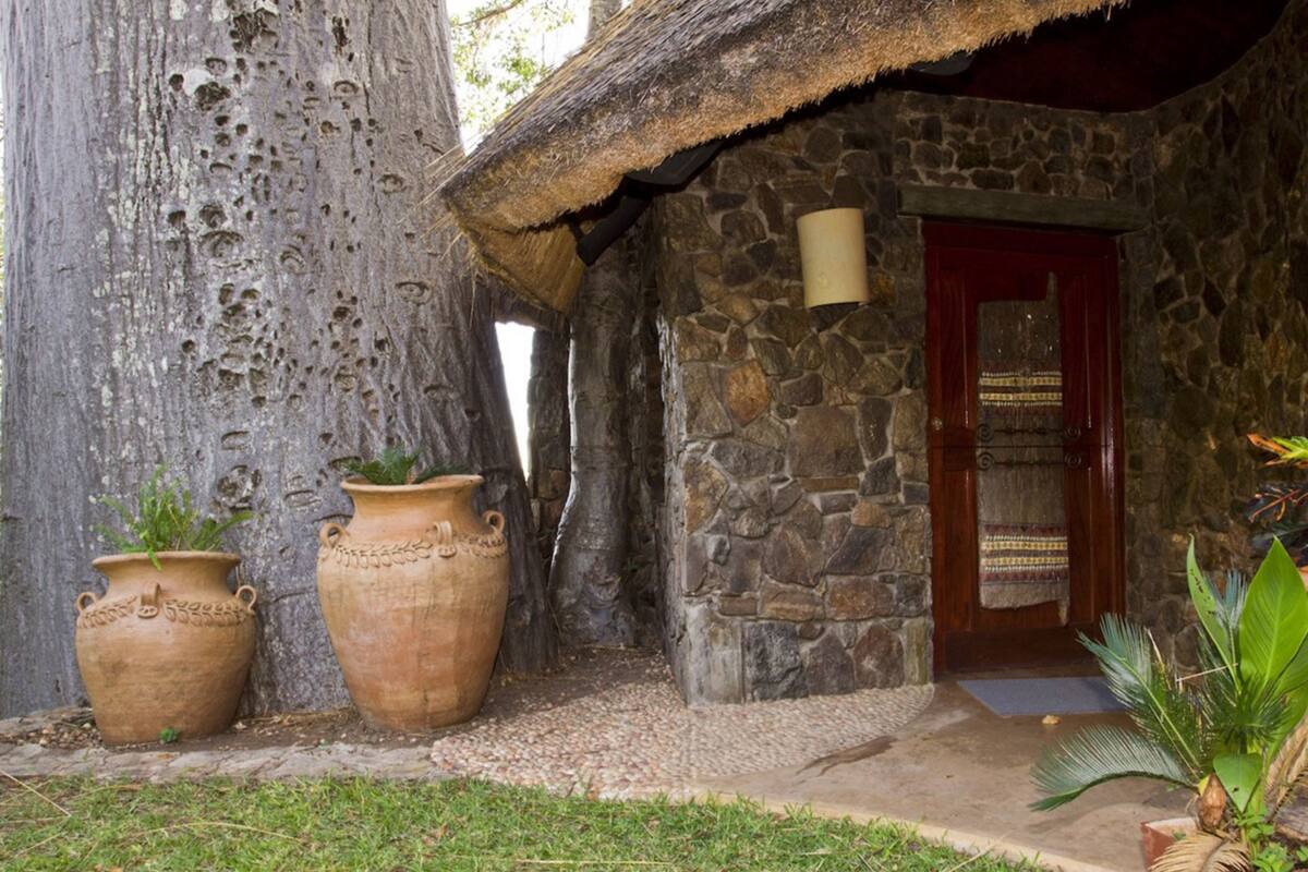 Un bâtiment rustique en pierre, avec un toit de chaume, deux grands pots en terre cuite et une porte en bois.