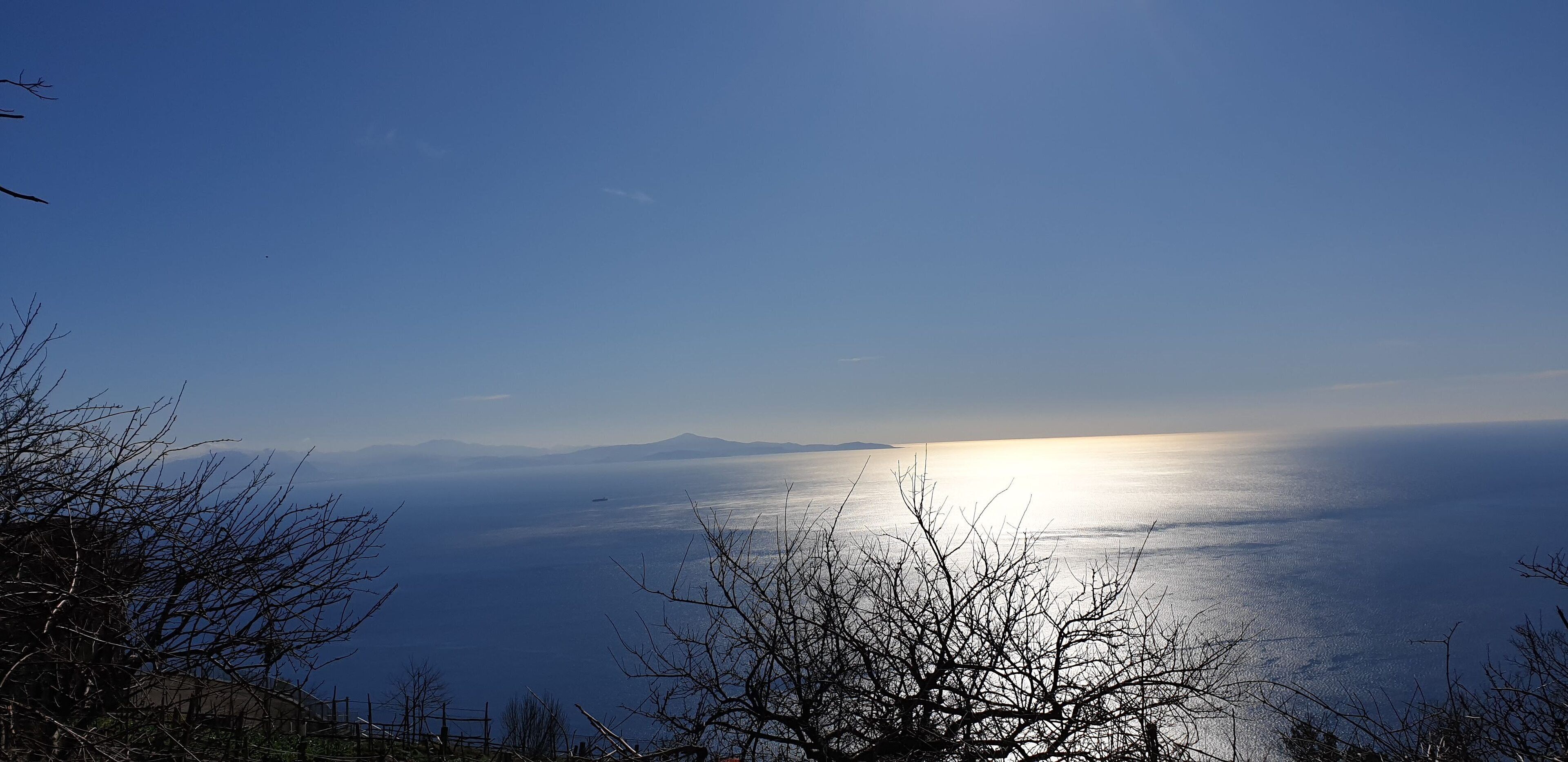 A coastal landscape with a clear view of the sea and distant mountains.