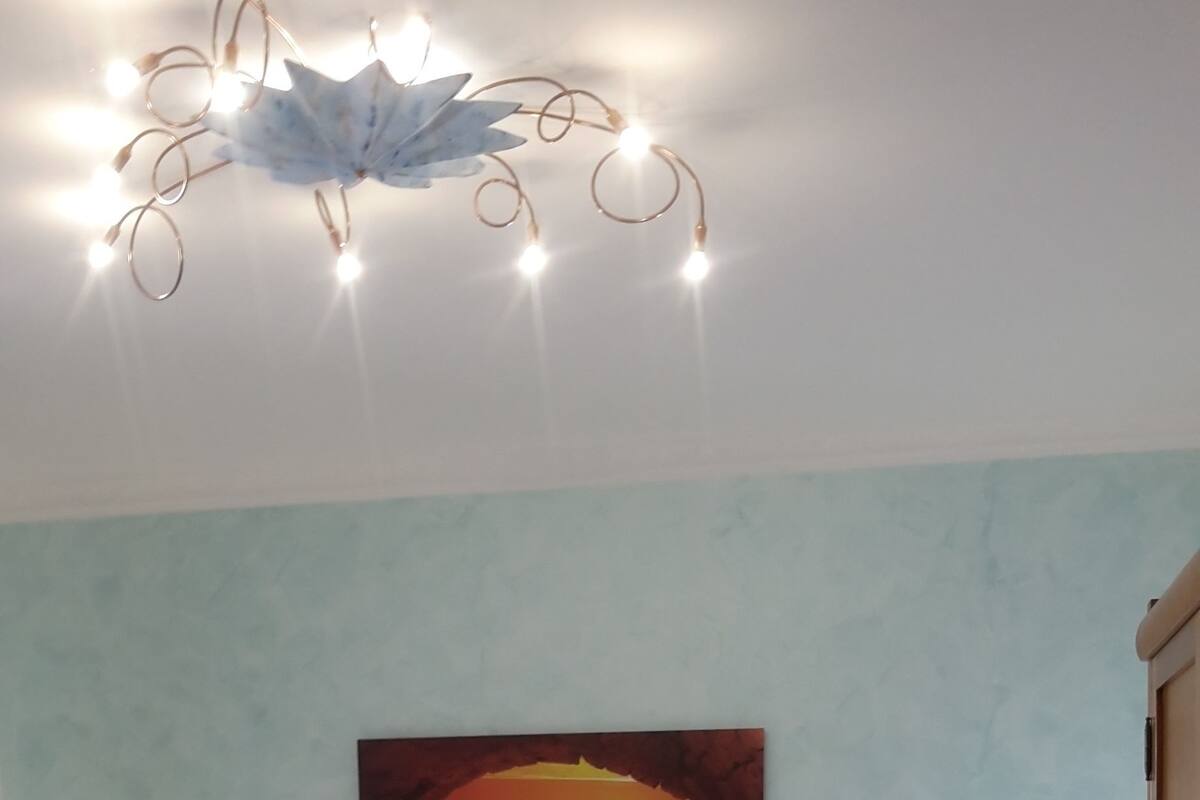 Une chambre à coucher comprenant un lit, deux tables de chevet, une commode, un luminaire fixé au mur et un tableau représentant un coucher de soleil.