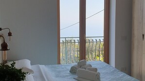 Une chambre à coucher avec un lit, une fenêtre donnant sur un beau paysage, une table de chevet avec une plante et une chaise en bois.