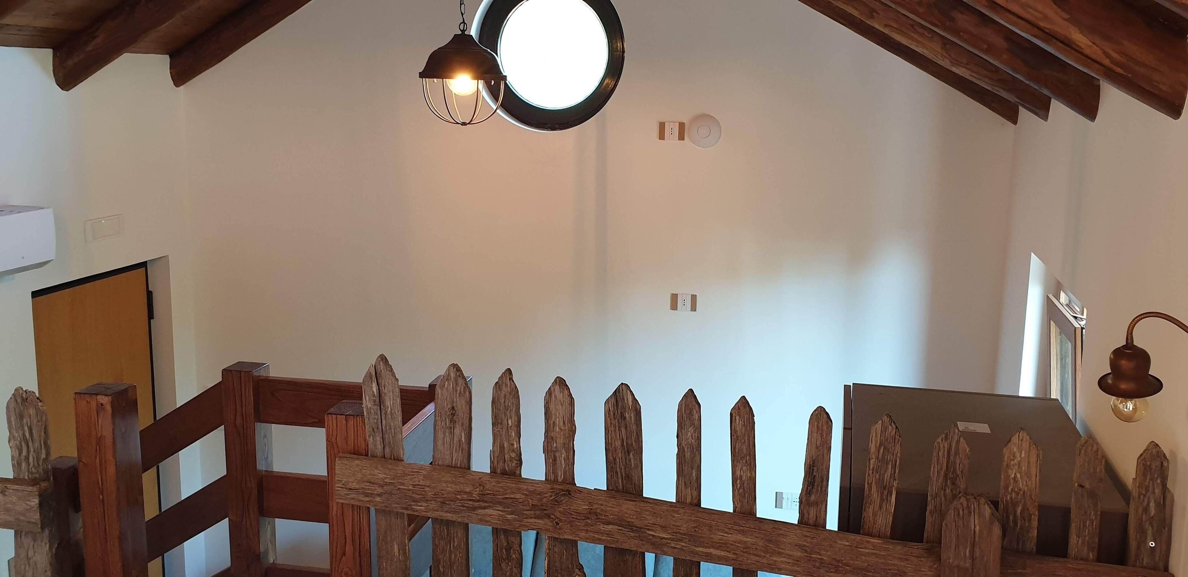 Un escalier en bois avec une rambarde rustique, un miroir rond et un luminaire fixé au mur.