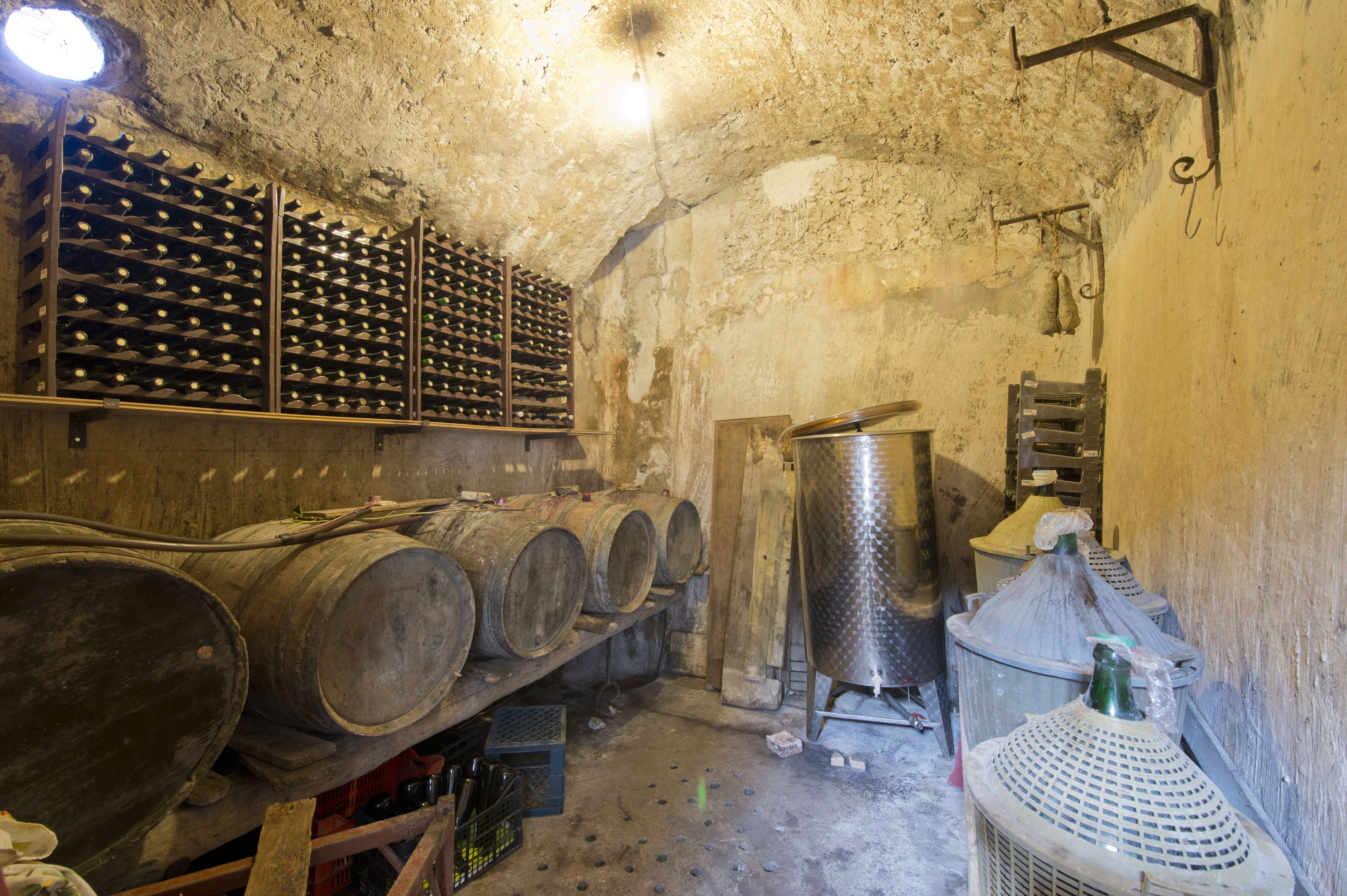 A cellar with wooden barrels, metal wine racks, and stainless steel fermentation tanks.