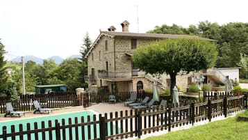 A stone building with a pool, surrounded by a wooden fence, and a tree in the foreground.