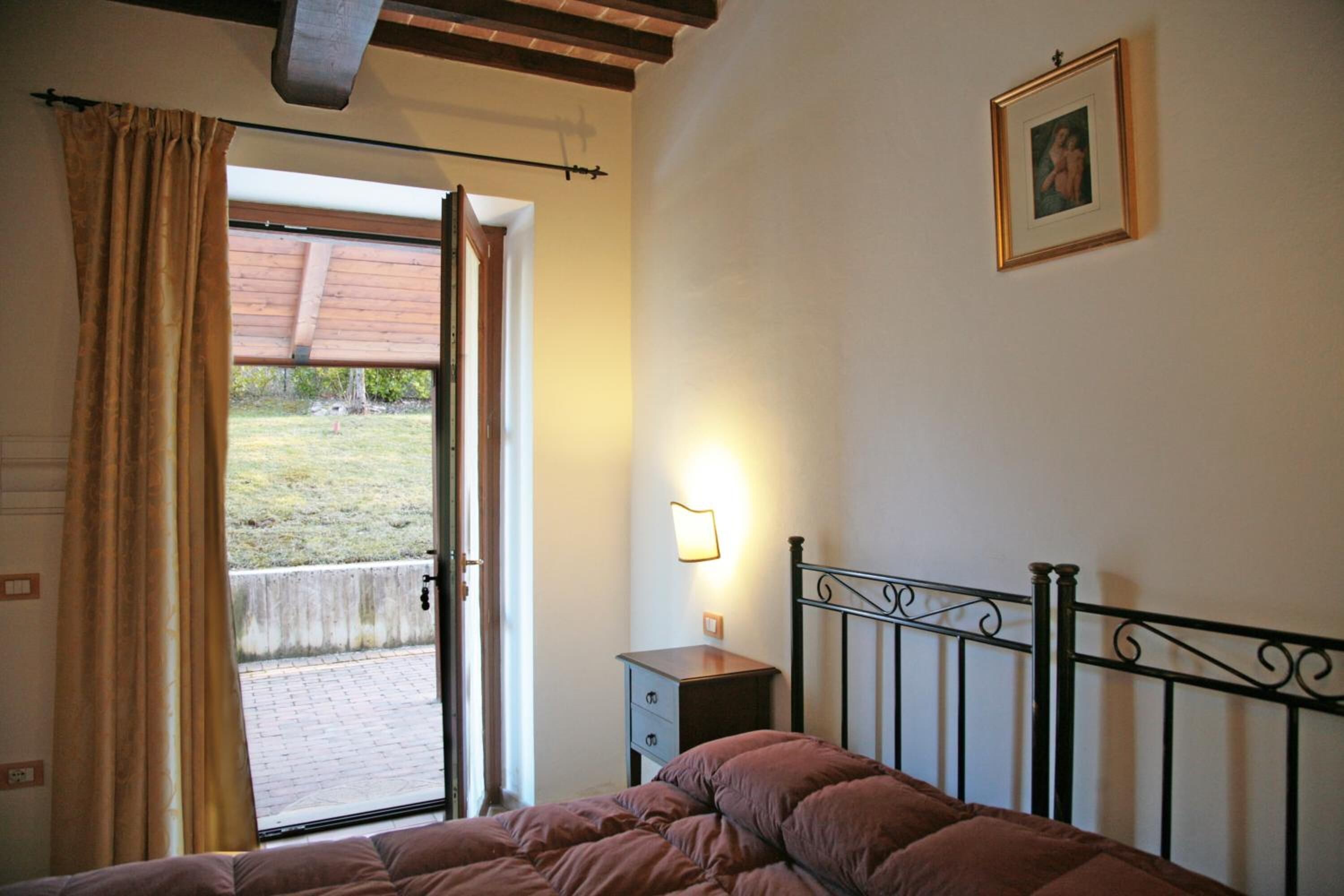 A bedroom with a bed, a nightstand, a wall-mounted lamp, a door leading to an outdoor area, and a framed picture on the wall.