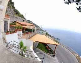 Una propiedad costera con terraza frente al mar, una escalera que lleva a un edificio y mobiliario exterior.