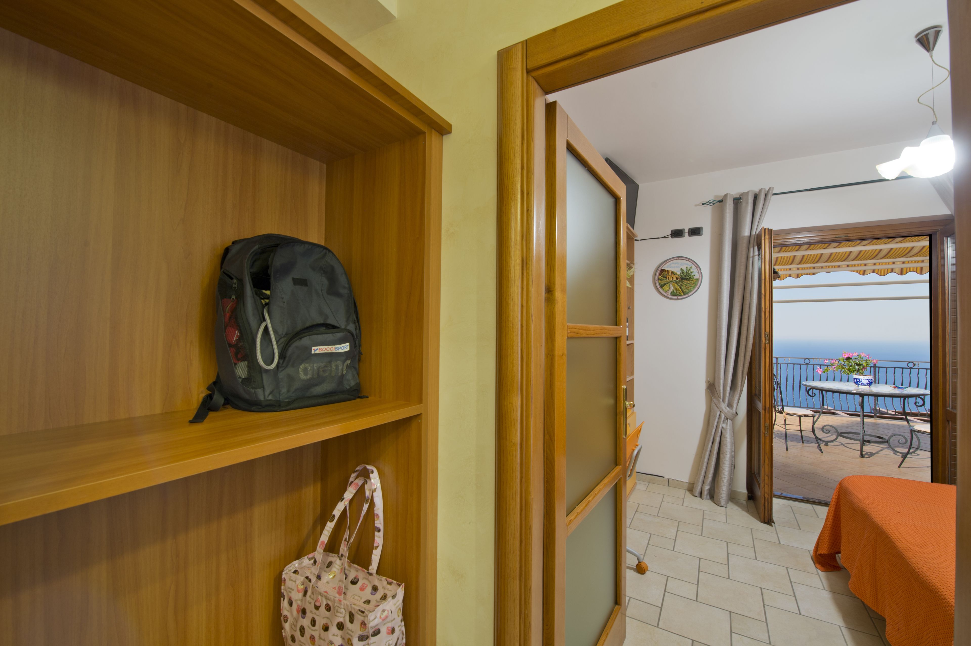 A room with wooden shelves, a table with an orange tablecloth, and a balcony with a view of the sea.