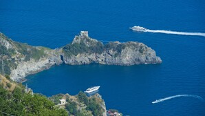 A coastal landscape with rocky cliffs, a small tower, and boats on the water. - La Mela Blu (Furore)