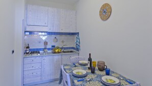 A compact kitchen with a blue and white color scheme, a sink, and a dining area with a table set for two. - La Mela Blu (Furore)