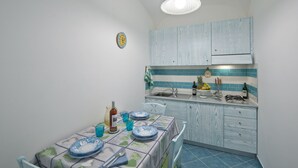 A compact kitchen with a dining area, featuring a sink, stove, and blue cabinetry. - La Mela Blu (Furore)
