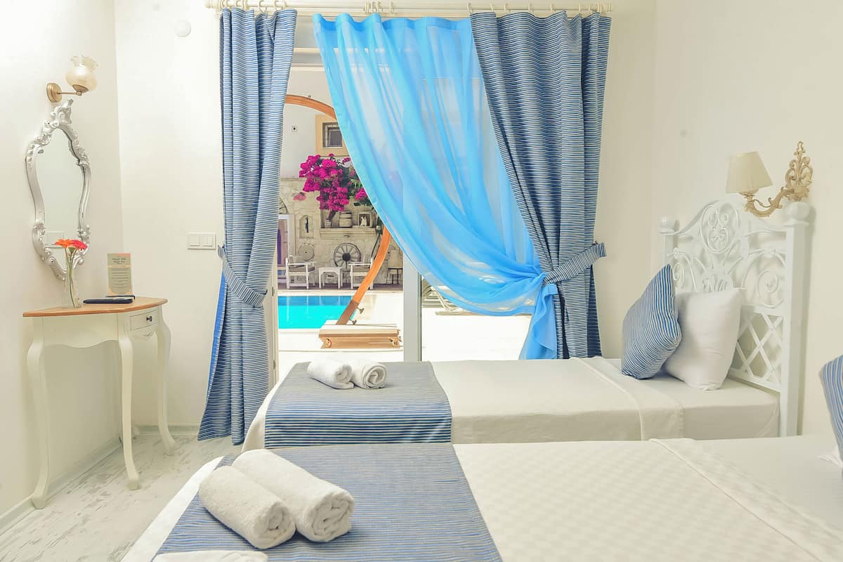 A hotel room with two beds, a small table, a mirror, and a view of a pool.