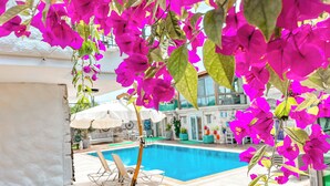 A poolside area with lounge chairs and an umbrella, surrounded by vibrant pink bougainvillea flowers. - Rüzgar Gülü Otel (Cesme)