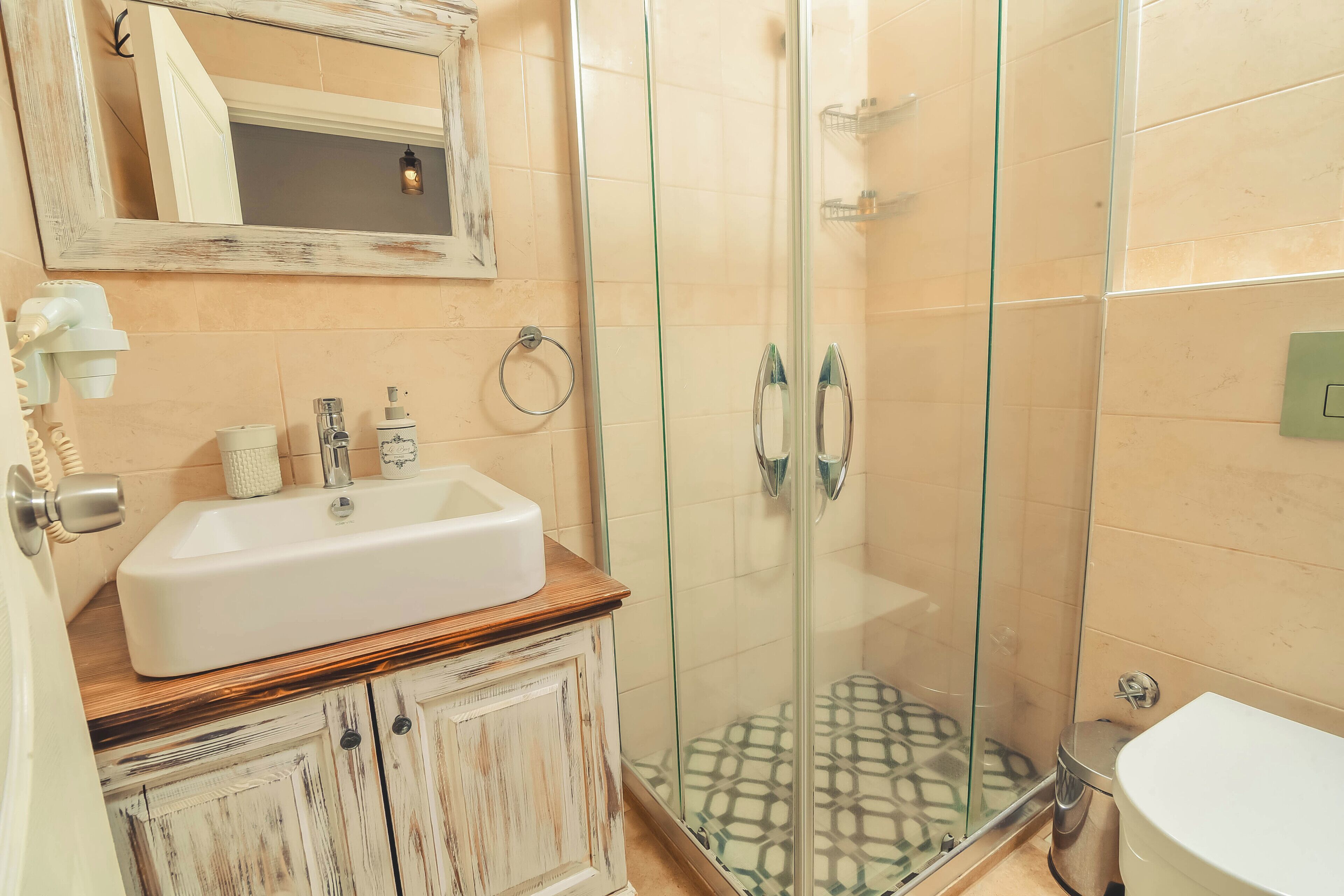 A bathroom with a white sink, wooden cabinet, glass shower enclosure, and a toilet.