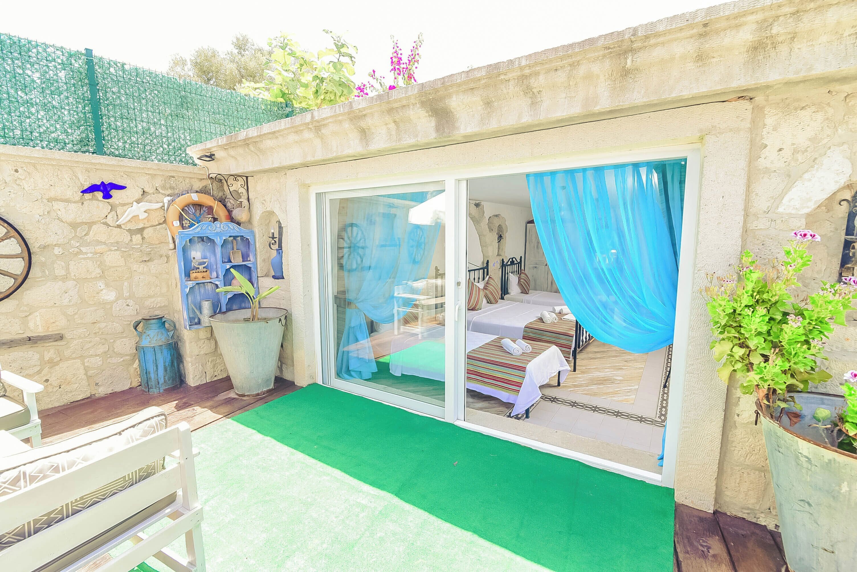 Una habitación con una cama, una ventana con cortinas azules, una mesita pequeña y una silla.