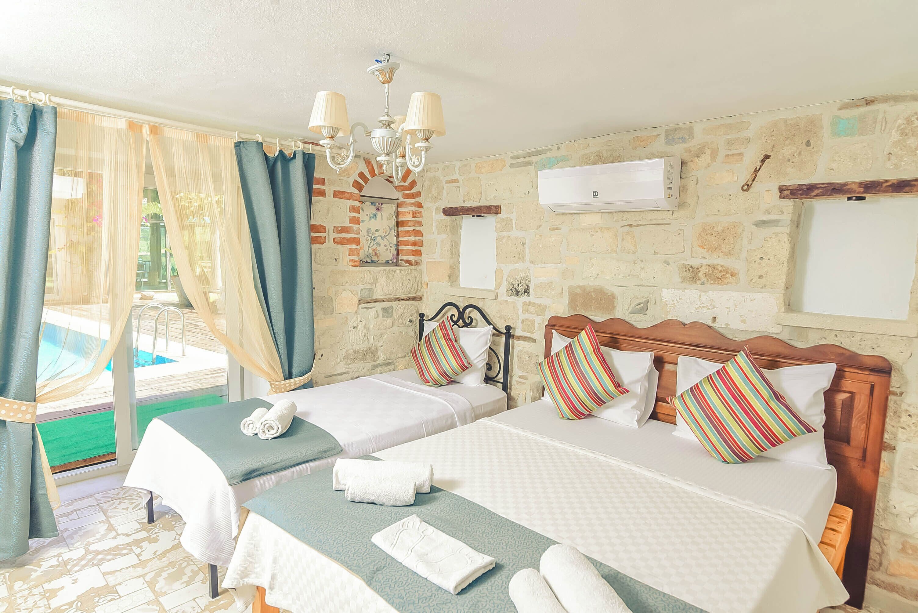 A hotel room with two beds, a chandelier, an air conditioning unit, and a stone wall.