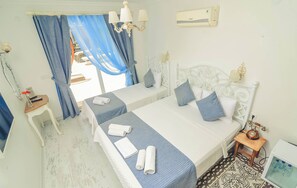 A hotel room with two beds, a small table, a chair, a desk, a lamp, a telephone, and a wall-mounted air conditioner. - Rüzgar Gülü Otel (Cesme)