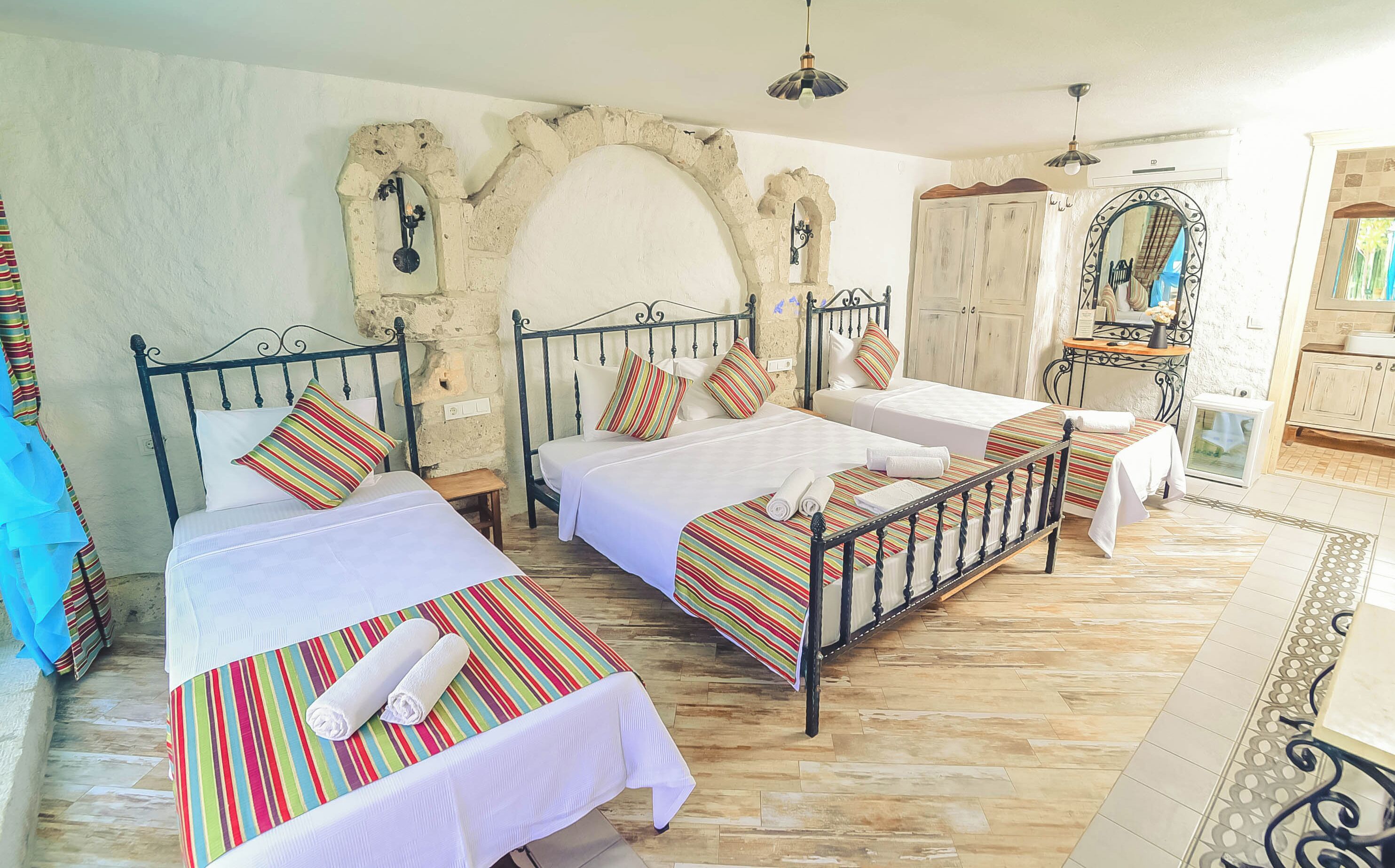 A room with two beds, each with a striped bedspread and white pillows, a wooden floor, and stone walls.