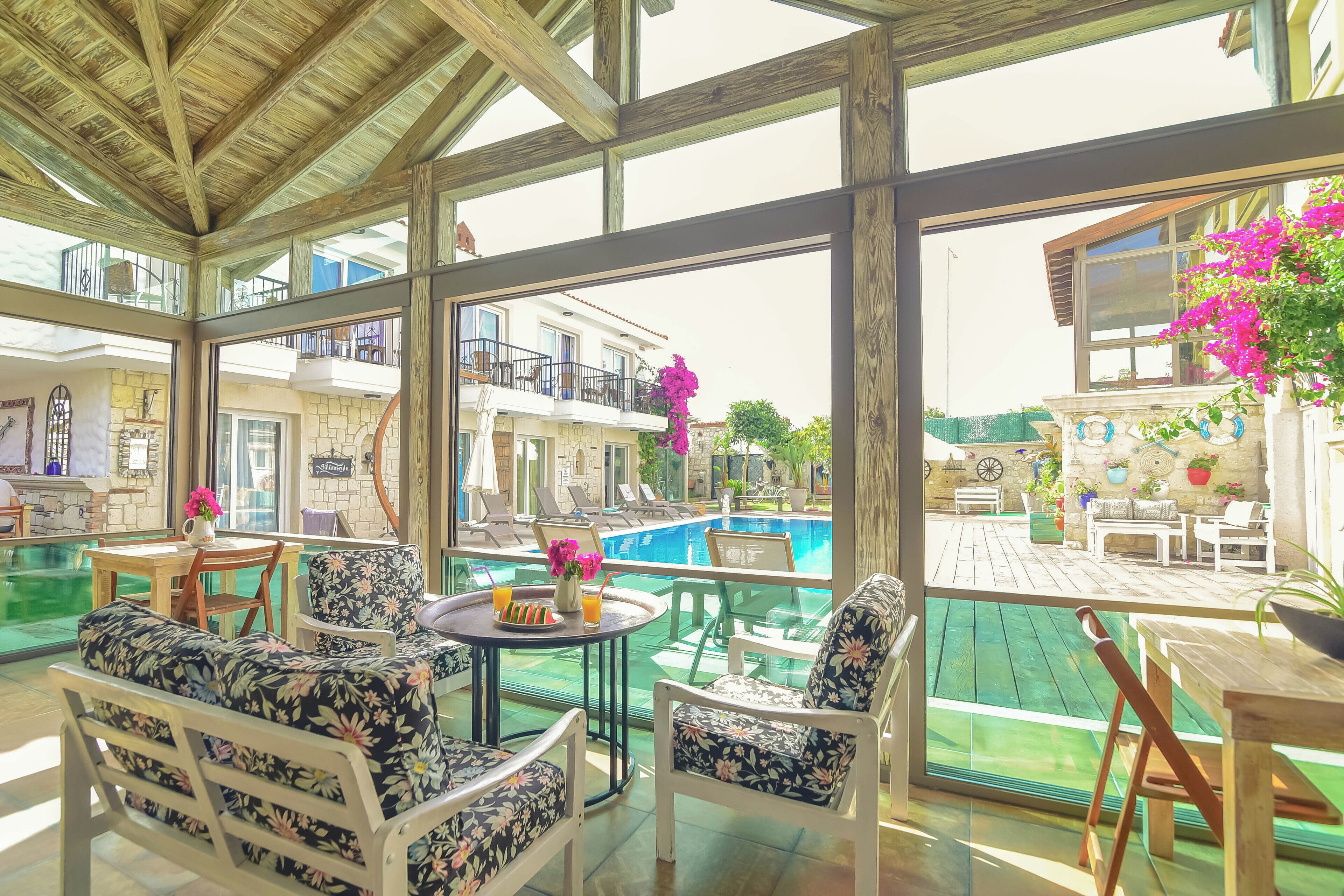 A covered outdoor seating area with a pool view, wooden furniture, and a stone wall.