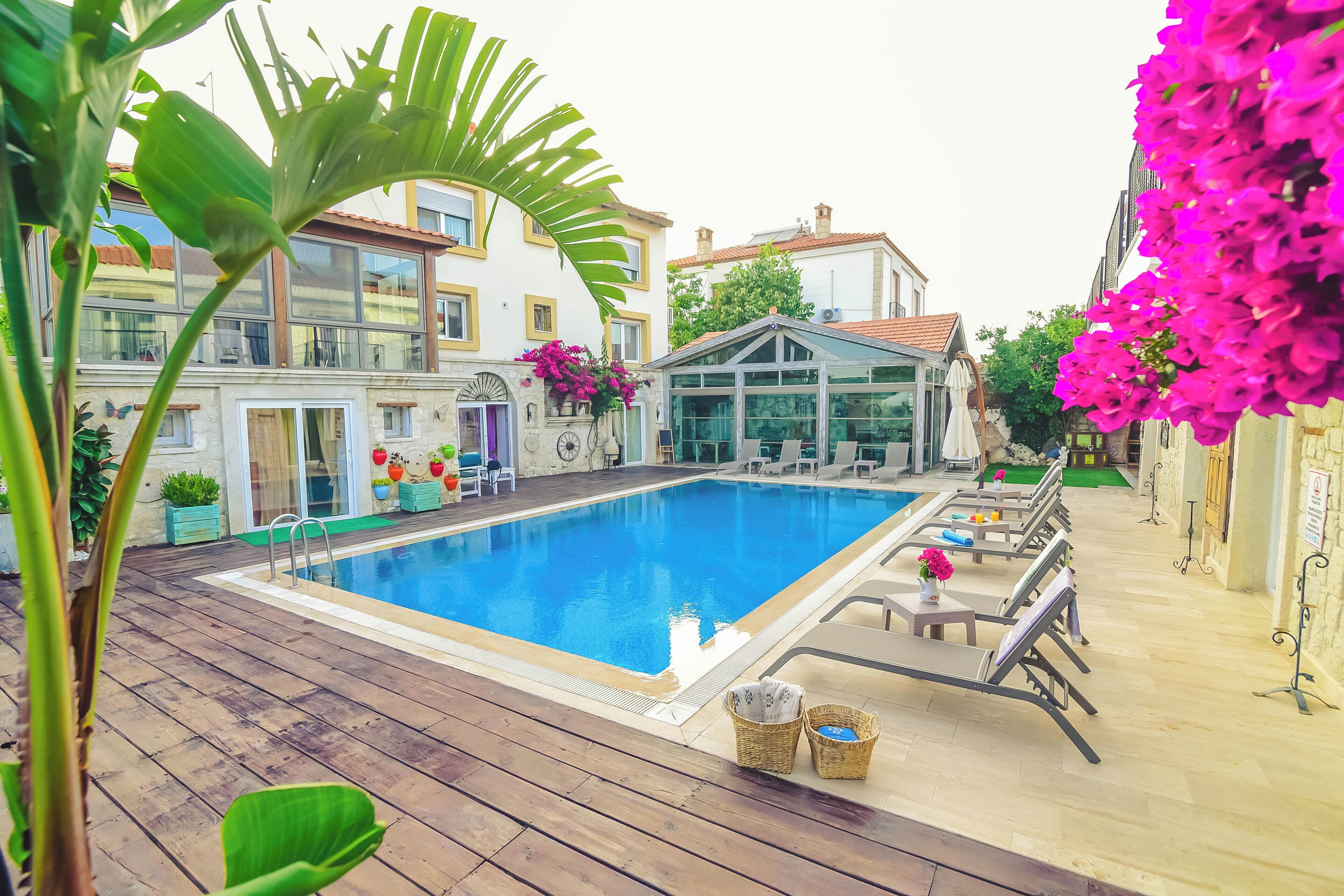 A swimming pool with lounge chairs and a glass-enclosed structure, surrounded by buildings and greenery.