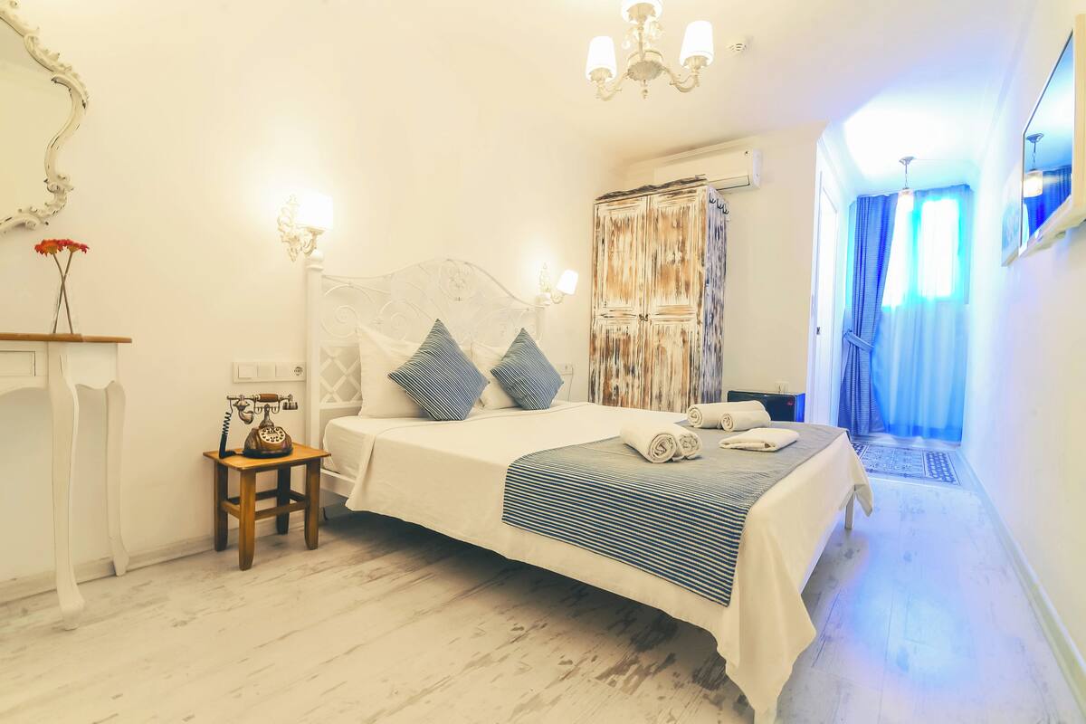 A bedroom with a large bed, a bedside table with a telephone, and a mirror on the wall.