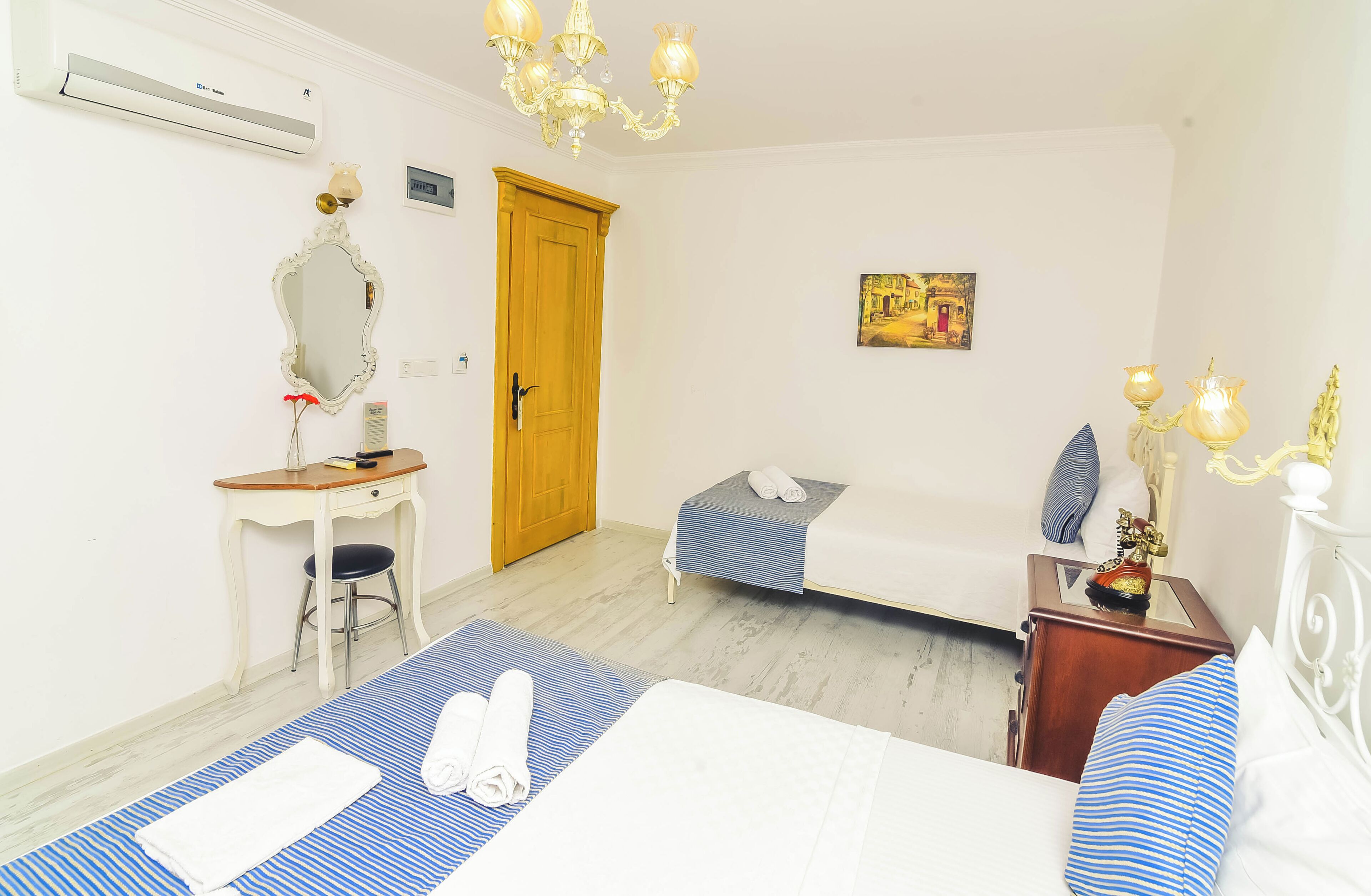 A hotel room with a bed, a desk, a chair, a wardrobe, and a chandelier.