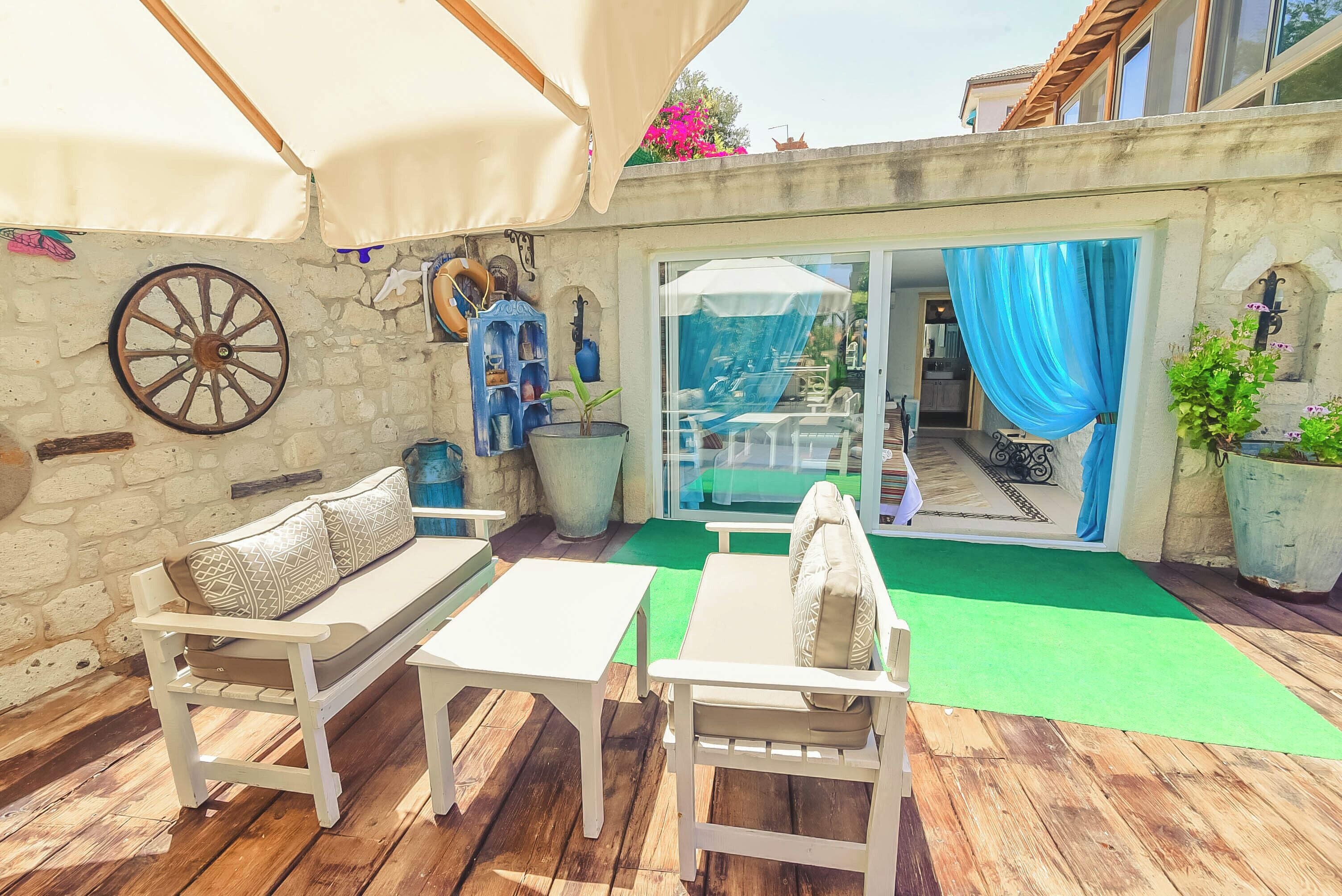 A patio with wooden furniture, a stone wall, and a large wheel.