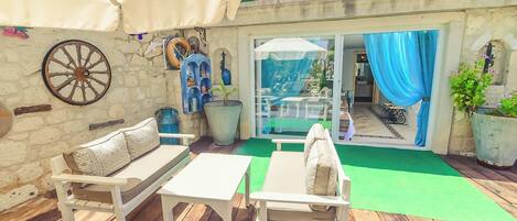 A patio with wooden furniture, a stone wall, and a large wheel.