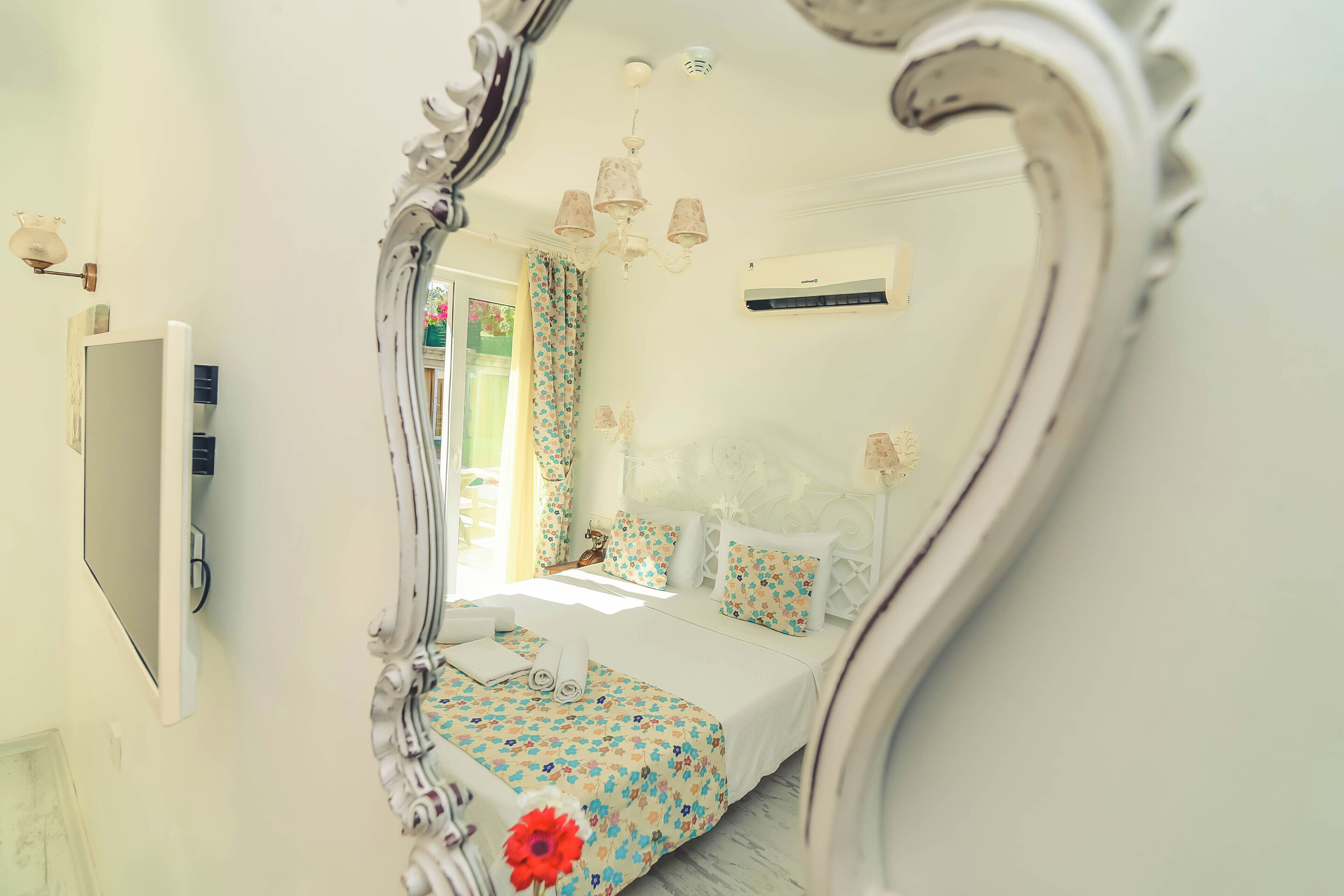 A bedroom with a large mirror, a bed with floral bedding, a chandelier, and an air conditioning unit.
