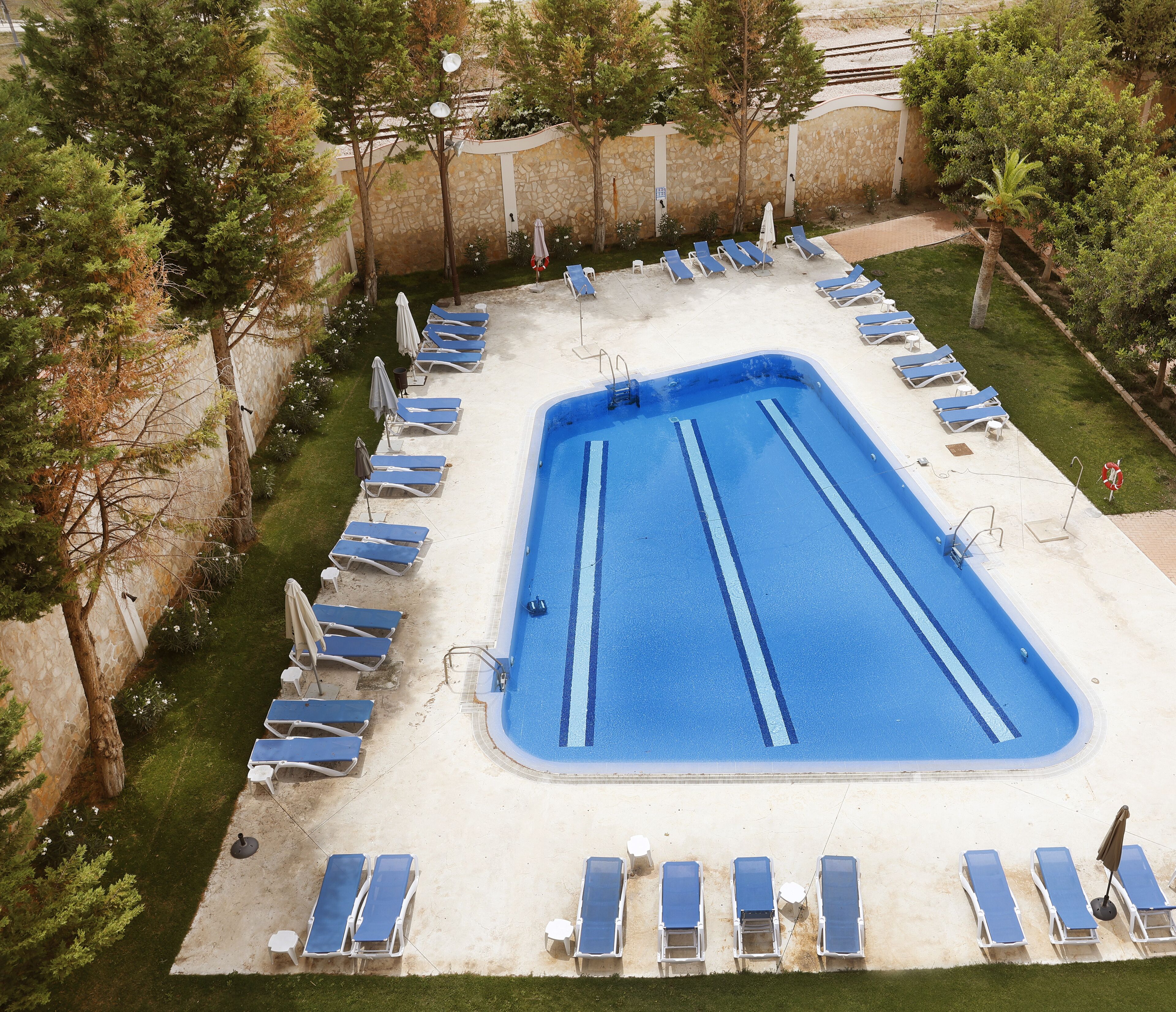Una piscina rectangular con divisiones azules para carriles, rodeada de sillas de descanso y sombrillas.