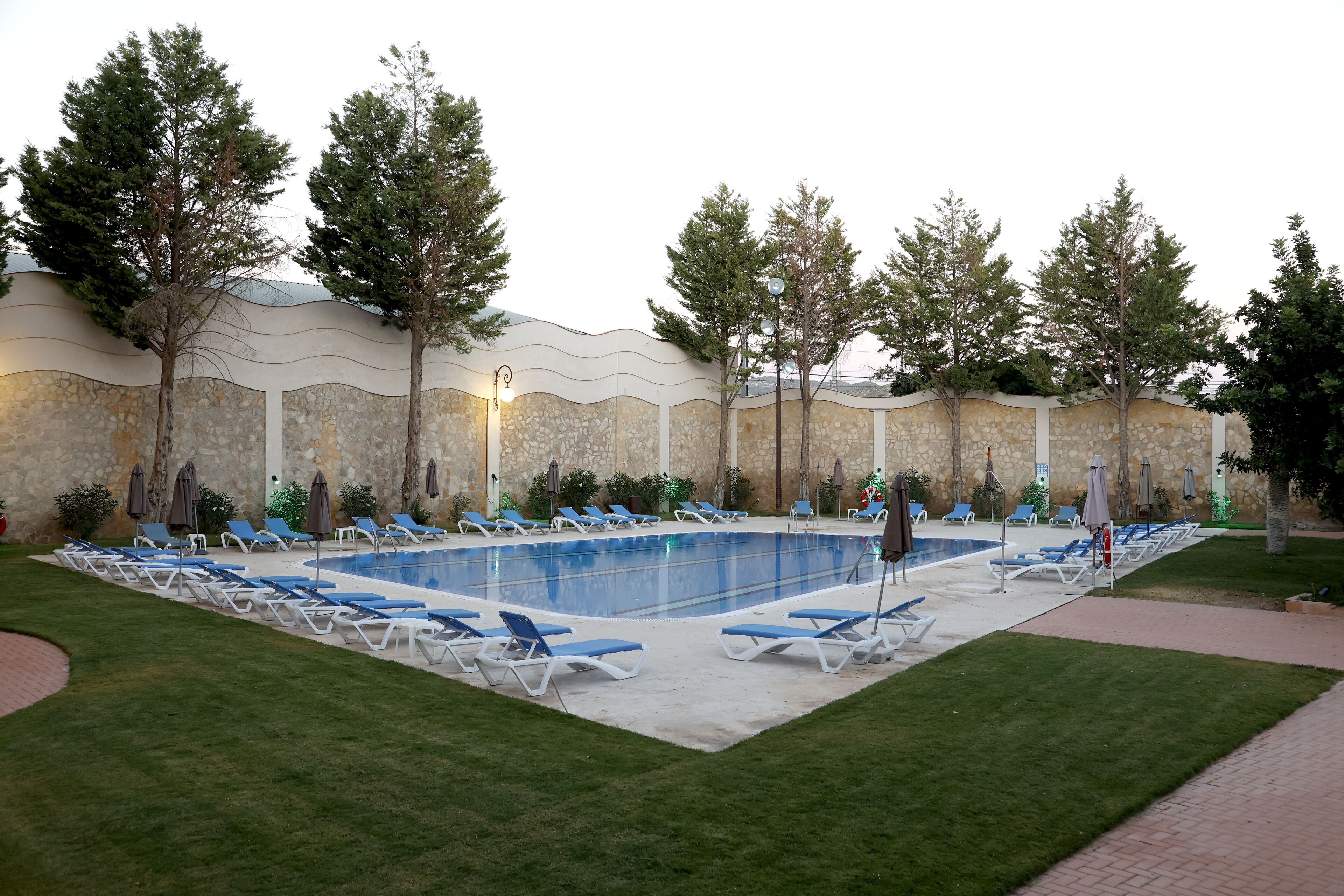 Piscina con sillas de descanso y un muro de piedra.