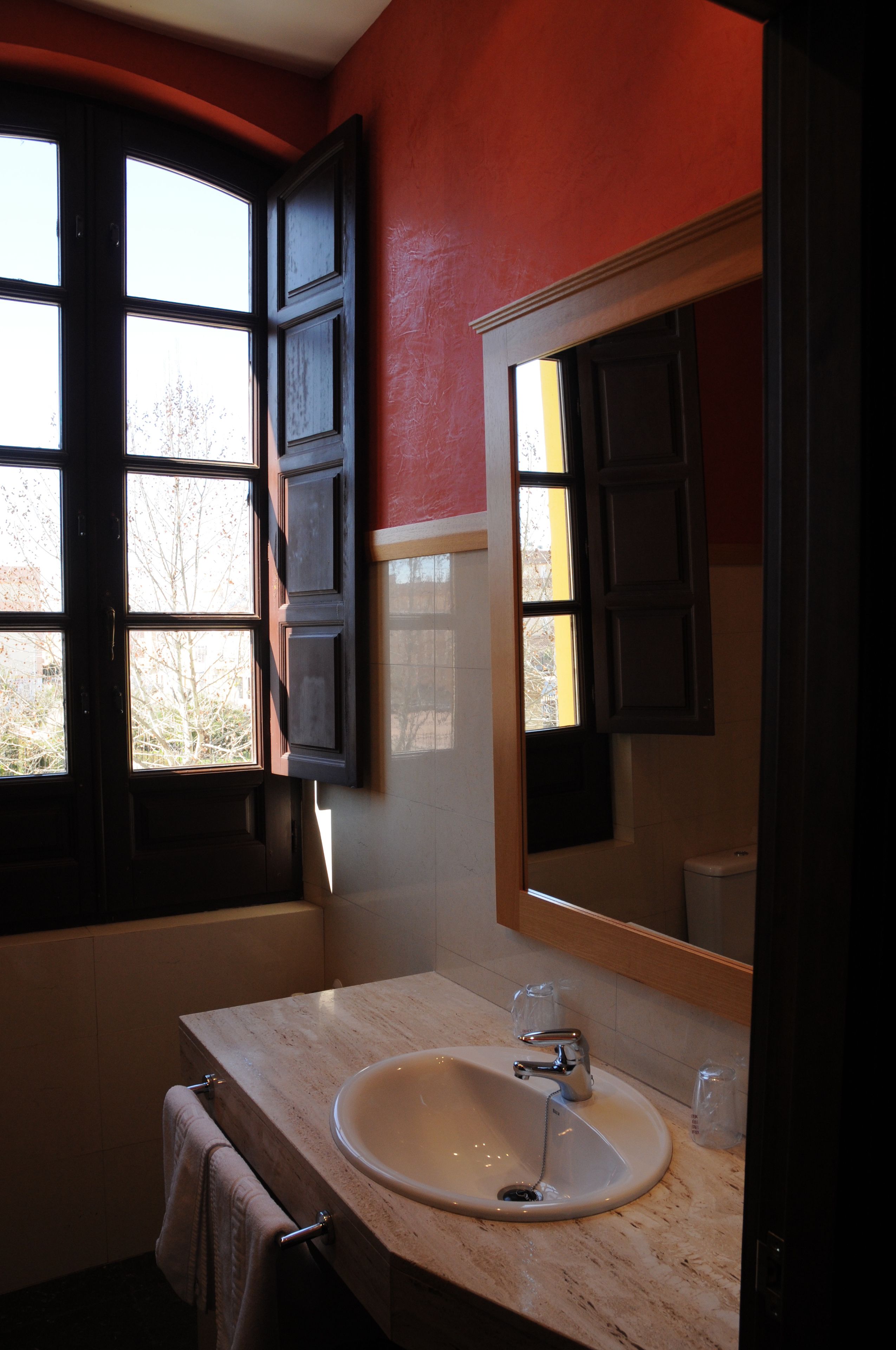 Une salle de bain avec un lavabo, un miroir et une fenêtre avec des rideaux.
