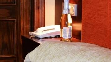 Een hotelkamer met een houten garderobe, een nachtkastje met een fles champagne, een telefoon en een bloemenboeket op het bed.