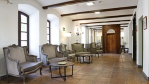 A spacious hallway with ornate chairs and tables, wooden beams on the ceiling, and a large wooden door at the end. - Hotel El Carmen (Puente Genil)