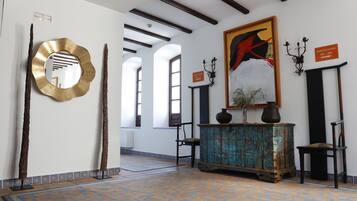 Un vestíbulo con alfombra estampada, un cuadro grande, un aparador antiguo y un letrero con los números de las habitaciones.